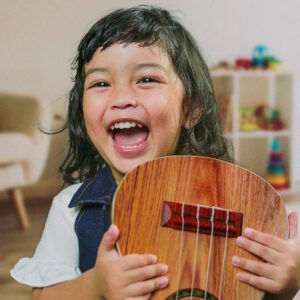 Jeder Mensch ist musikalisch | ein lachendes Mädchen mit dunklen Haaren hält ein Musikinstrument in der Händen